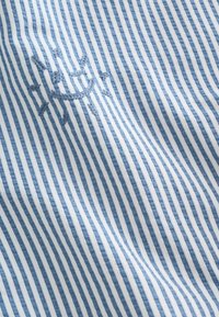Tissu à rayures verticales bleues et blanches avec un petit détail brodé d'un soleil souriant en fil bleu.
