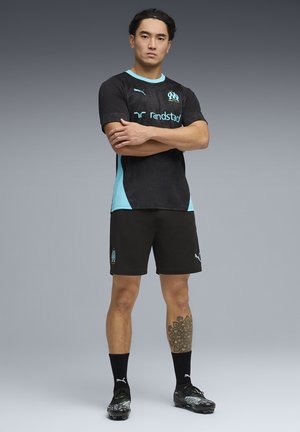 Schwarzes Fußballtrikot mit türkisfarbenen Akzenten und Logo, kombiniert mit schwarzen Shorts. Verfügt über kurze Ärmel, strukturierten Stoff und athletische Passform.