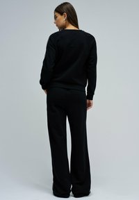 Sweatshirt noir et pantalon large assorti en tissu doux, avec un col rond et des manches longues à poignet côtelé.