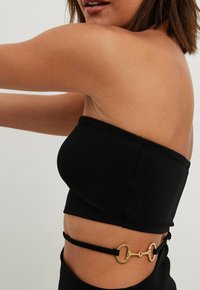 Černý bezramenný top s přiléhavým střihem. Obsahuje zlatý kulatý kovový detail a nastavitelné boční popruhy pro bezpečné nošení.