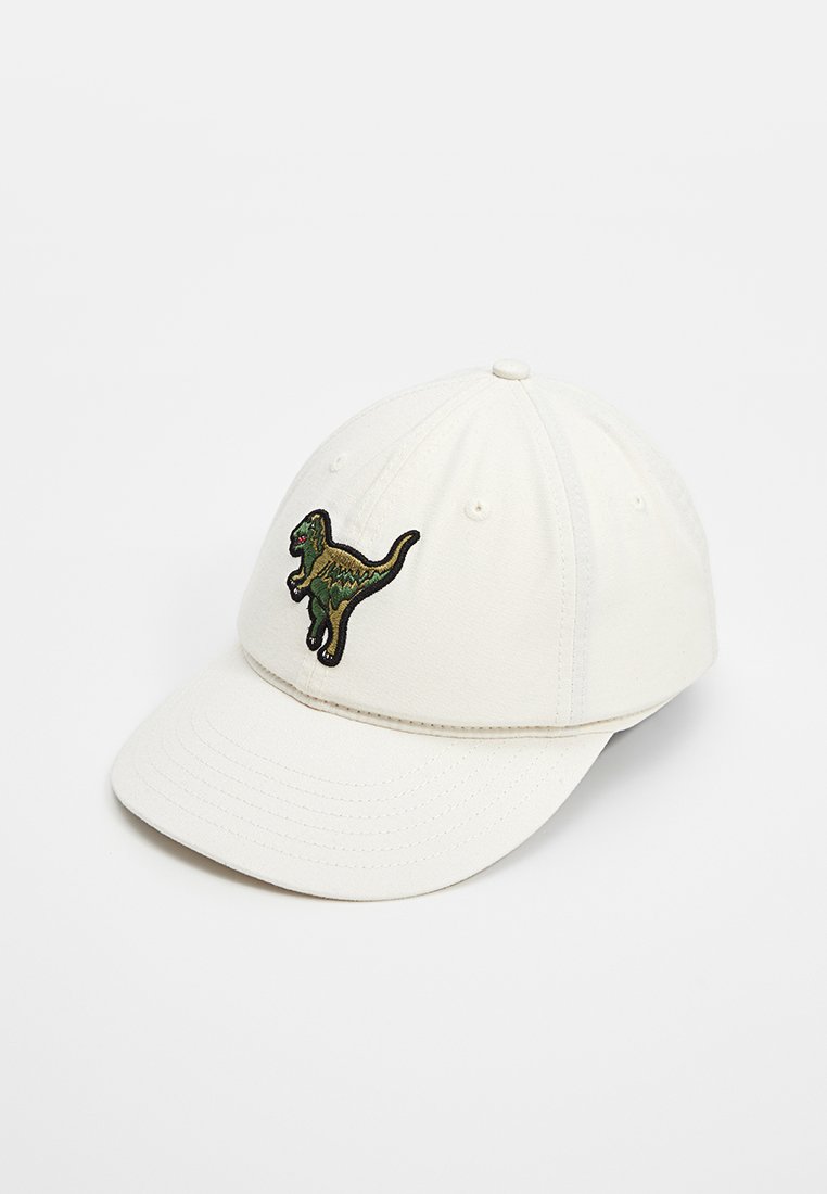 Casquette en coton blanc avec une visière courbée et un dinosaure vert brodé sur le devant. Présente des détails cousus et des trous de ventilation.