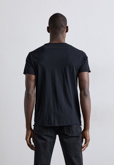 Camiseta de algodón negra con mangas cortas y cuello redondo, mostrada desde la parte de atrás, presenta un corte holgado y una textura suave.