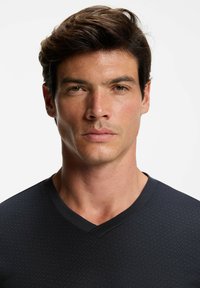 Czarna koszula z dekoltem w serek o fakturowanym wzorze, gładkiej tkaninie i dopasowanym kroju, prezentowana na męskim modelu z krótkimi, potarganymi włosami.