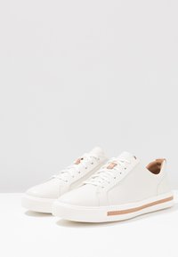 Weiße Ledersneaker mit glatter Oberfläche, runder Zehenpartie und minimalistischem Design. Beige Akzente an der Zunge und der Seitennaht. Gummisohle.