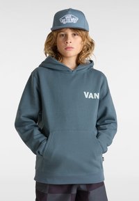 Sudadera teal con bolsillo frontal y logo "VAN". Combinada con una gorra azul clara que presenta el logo "VANS OFF THE WALL". Casual, de tela suave.
