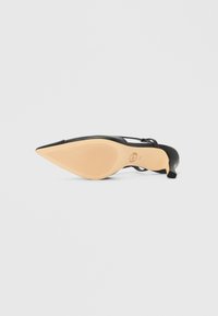 Musta kärjestään teräväkärkinen kenkä, jossa on sileä nahkapäällinen, ohut nilkkahihna ja beige, vaakasuorilla urilla ja brändäyksellä kuvioitu pohja.