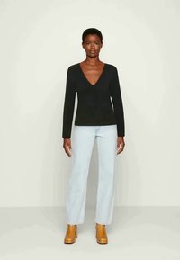 Top preto de mangaslongas com decote em V, combinado com jeans de perna larga azul claro e botas cano curto de salto grosso castanhas. Textura suave.