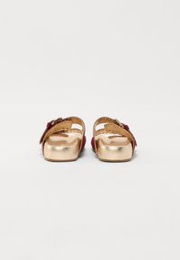 Sandales en daim rouge avec une base métallisée dorée, dotées de deux lanières réglables, d'un bout rond et d'un design à plateforme surélevée.