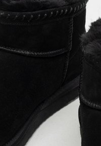 Czarne zamszowe botki do kostki z miękką futrzaną wyściółką, z przeszywanym szwem i płaską gumową podeszwą, prezentujące gładką teksturę i monochromatyczny design.