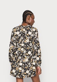 Vestido floral preto com flores amarelas e brancas. Apresenta mangas longas e um decote franzido. Tecido leve com um corte ligeiramente solto.