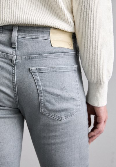 Slim-fit, gray denim jeans with a beige leather patch at the waistband. Features back pockets with subtle stitching detail.