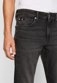 Los jeans de mezclilla negra presentan un diseño clásico de cinco bolsillos, un sutil desgastado y una pequeña etiqueta con el logotipo en el bolsillo delantero. Tejido texturizado y corte recto.