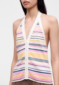 Femme portant un top sans manches à col halter boutonné avec des rayures horizontales roses, jaunes, bleu marine et blanches sur un tissu en maille côtelée.