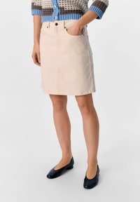 Lichtroze denimrok met een aangesloten taille, voorzakken en een rechte snit, gecombineerd met zwarte schoenen met een lage hak.