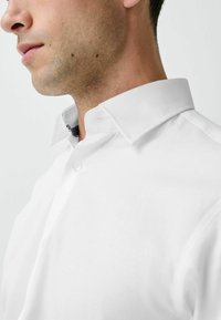 Weißes Hemd mit strukturiertem Kragen, das eine subtile Textur und einen grauen Akzent unter dem Kragen aufweist. Sauberes, maßgeschneidertes Design.