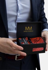 Conjunto de gemelos y corbata en una caja negra. Corbata de patrón rojo, gemelos de hardware plateado. La caja presenta el logo dorado "MASSI MORINO." Presentación elegante.