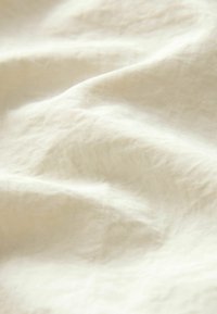 Linneduge i en blød, off-white nuance, der fremhæver en tekstureret overflade med bløde folder og subtile vævemønstre.