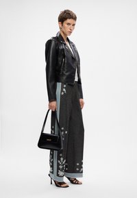 Veste de motard en cuir noir sur un haut blanc, associée à un pantalon large noir étincelant arborant des broderies florales et des bandes latérales bleu clair. Porte un sac à main noir.