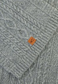 Grå strikket sweater med kabelmønstre, ribbede manchetter og et læderlogo-patch. Teksturen er chunky med et let fuzzy udseende.