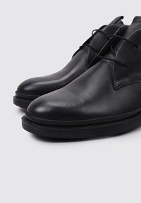 Zapatos de cuero negro con un acabado suave, punta redonda, diseño minimalista y cordones. Cuentan con una suela de goma baja para mayor comodidad.