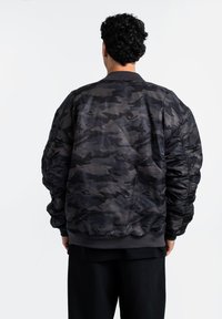 Giacca bomber in un motivo camouflage nero e grigio, con colletto a costine, polsini elastici e una texture leggermente imbottita.