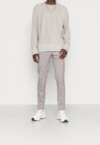 Light gray pullover sweater with a soft texture, paired with slim-fit checkered trousers in beige and brown, and white athletic sneakers.