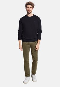 Czarny sweter dzianinowy, khaki chinosy, białe trampki. Prosty, dopasowany krój z prążkowanymi mankietami i pasem. Gładka faktura, swobodny styl.