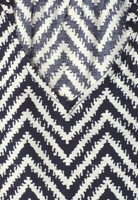 Vêtement à col en V avec motif en zigzag dentelé bleu marine et blanc créant un design chevron audacieux.