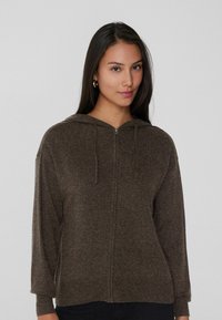 Sudadera con cremallera en color marrón con una textura suave, que cuenta con capucha, cordones y mangas largas. El diseño incluye una cremallera frontal y puños acanalados.