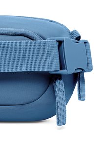 Sininen kangaspussi, jonka pinta on sileä. Pussissa on kestävä hihna ja muovinen solki. Yhdellä puolella on näkyviä ompeleita ja kaareva muoto.