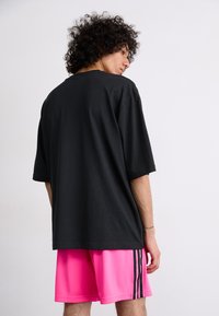 Sort oversized T-shirt med korte ærmer, kombineret med lyserøde shorts med sorte striber langs siderne. Glat bomuldsstruktur.