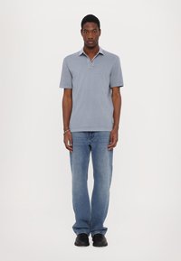 Light blue polo shirt with a collar, paired with faded blue straight-leg jeans and black shoes, standing against a plain white background.