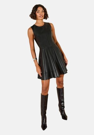 Schwarzes, ärmelloses Lederkleid mit schwingendem Saum, das eine glatte Textur und ein einfaches Design aufweist; kombiniert mit knielangen, schwarzen Stiefeln.