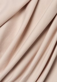 Miękki beżowy materiał z gładkimi, równomiernie rozmieszczonymi fałdami, które podkreślają jego delikatną fakturę i subtelny układ.