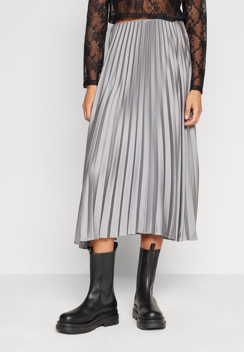 Jupe midi plissée en tissu argenté avec une texture lisse, associée à des bottines noires à semelle robuste et à design droit.