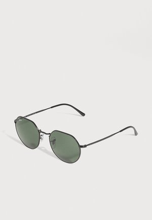 Lunettes de soleil à monture métallique noire, avec des verres ronds verts et des plaquettes nasales transparentes, sur un fond uni.