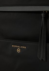 Čierny nylonový batoh s hladkým povrchom, zlatým logom a zipsovým vreckom s koženým strapcom.