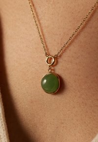 Collier en or avec un pendentif rond en jade vert, suspendu à une chaîne délicate avec un anneau circulaire reliant le pendentif à la chaîne.