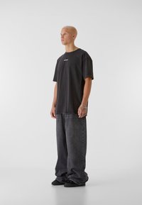 Tmavě šedé oversized bavlněné tričko s malým logem, doplněné volnými šedými džíny a černými teniskami. Jednoduchý, pohodlný design.