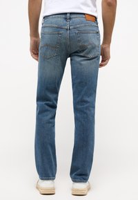 Blå denimjeans med rak benmodell, orange sömmar på midjan och fickorna samt en läderlapp på baksidan.