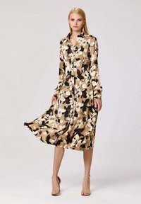 Robe à manches longues de couleur beige avec un imprimé floral en noir et blanc. Fabriquée en tissu doux, avec une fermeture à boutons sur le devant et une jupe fluide.