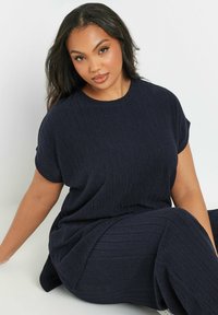 Laivansinis, teksturoitu kahden osan asu, joka koostuu löysästä lyhythihaisesta paidasta ja leveälahkeisista housuista, joissa on uurteinen kuvio. Pehmeä kangaspinta.