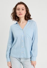 Light blue button-up shirt with long sleeves, soft fabric, a chest pocket, and a collar. Features white buttons and a relaxed fit.