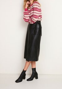 Falda midi de cuero negro con abertura lateral; combinada con un suéter rosa de patrón y botas negras de tobillo con tacones cuadrados. Textura suave, diseño clásico.