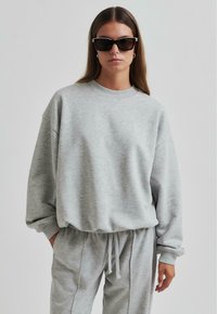 Sudadera gris claro de gran tamaño con cuello redondo y mangas largas, combinada con pantalones jogger gris a juego con cintura ajustable.