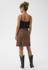 Jupe en cuir marron à coupe droite, avec deux poches arrière. Associée avec un haut noir et des bottes de cowboy noires.