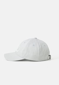 Lys grå baseball caps med buet brem, ventilasjonsøyler, justerbar stropp og liten brodert logo på siden.