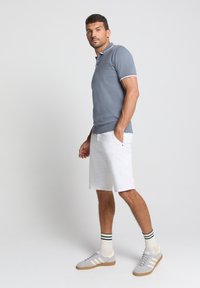 Lichtgrijze polo met witte accenten, gecombineerd met witte shorts. De outfit heeft een gestructureerd materiaal en grijze sneakers met witte strepen.