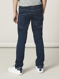 Mørkeblå jeans med slim fit, som har to baklommer, kontraststing og minimalt med detaljer. Brukt med hvite sneakers.