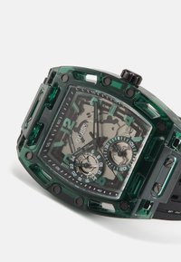 Reloj de resina transparente verde con caja rectangular, acentos negros, dos subesferas y un dial con patrón de camuflaje. Presenta números grandes.